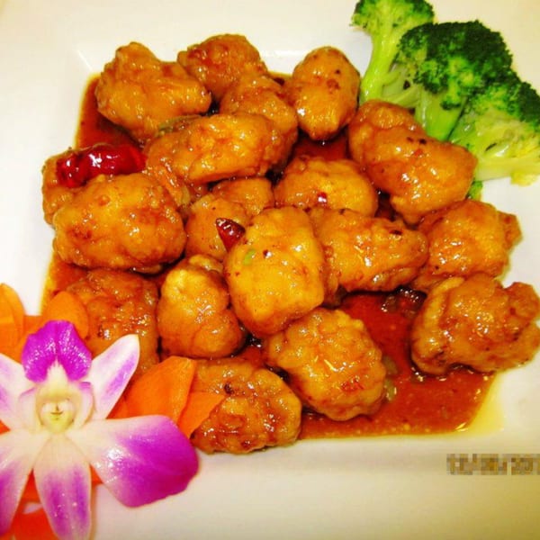Sweet and sour chicken with broccoli florets and an orchid garnish on a white plate.
