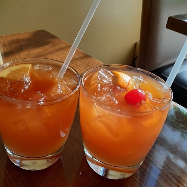Two orange cocktails with ice, orange slices, and a cherry, on a wooden table at Sushi Joy.