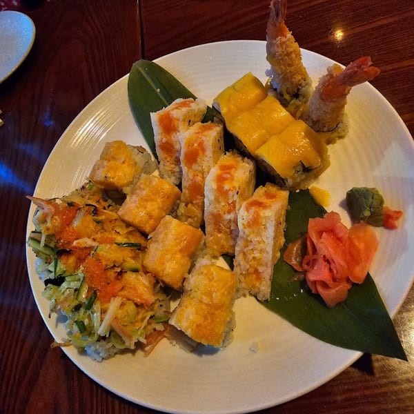 A white plate of various sushi rolls, including tempura shrimp, on a dark wooden table.
