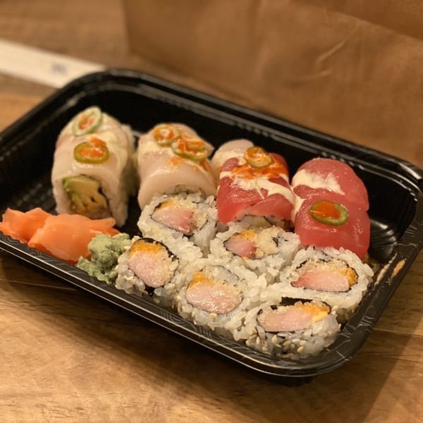 A black tray of Sushi Joy's sushi rolls, including tuna, yellowtail, and salmon, with ginger and wasabi.